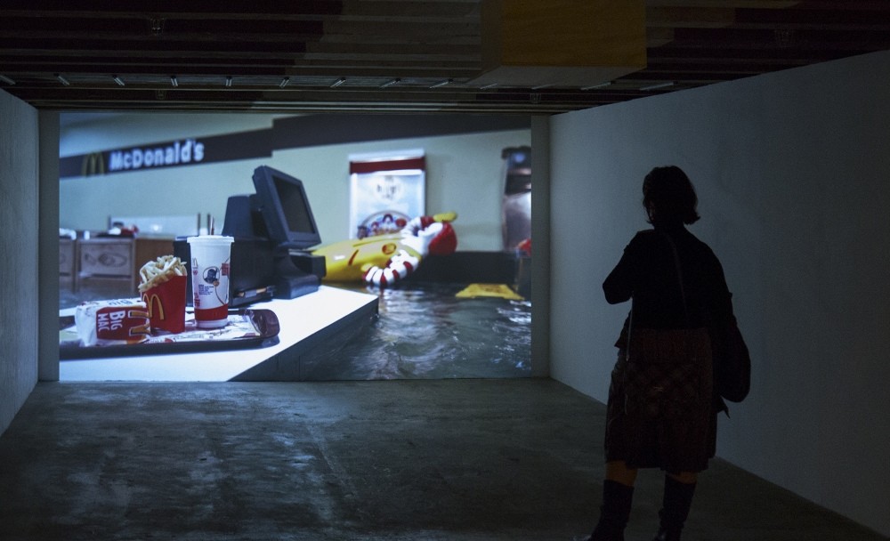 In u201cFlooded McDonaldu2019s,u201d we see hamburgers, french fries, coke, toys floating, passing by camera, as well as the restaurantu2019s furniture. Towards the end, when everything is submerged and image of video becomes blurry, everything becomes obscured. 