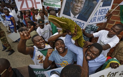 Supporters of Mnangagwa hold a stuffed crocodile and pictures of him as they cheer at Manyame Air Force base in Harare, Zimbabwe Nov. 22, 2017. (AP Photo)