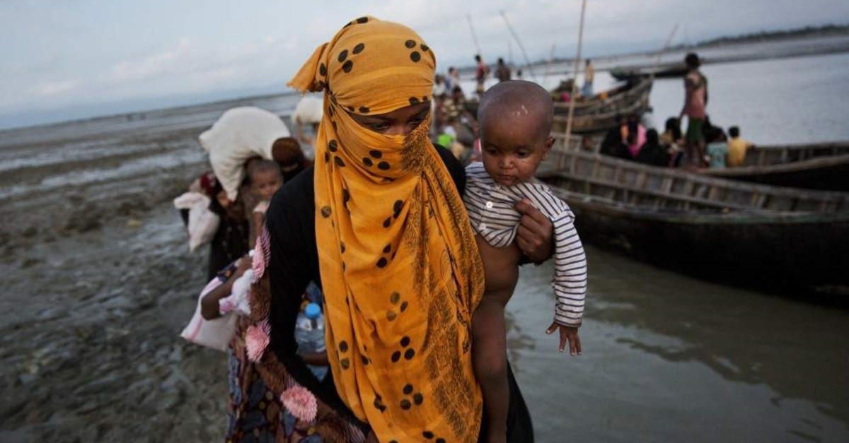 In this Sept. 21, 2017 photo, a Rohingya woman carries a child after crossing a stream on a small boat near Cox's Bazar's Dakhinpara area, Bangladesh. (AP Photo)